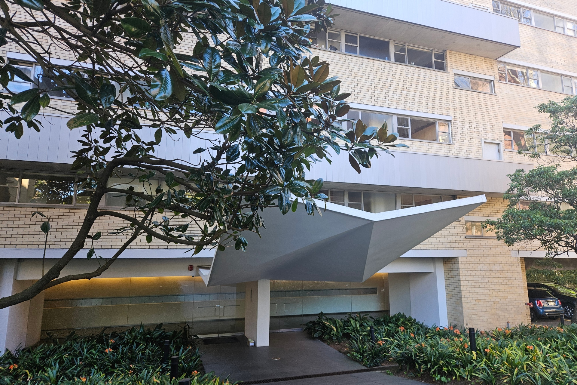 The front entrance of a large brick apartment complex in a tree-lined street