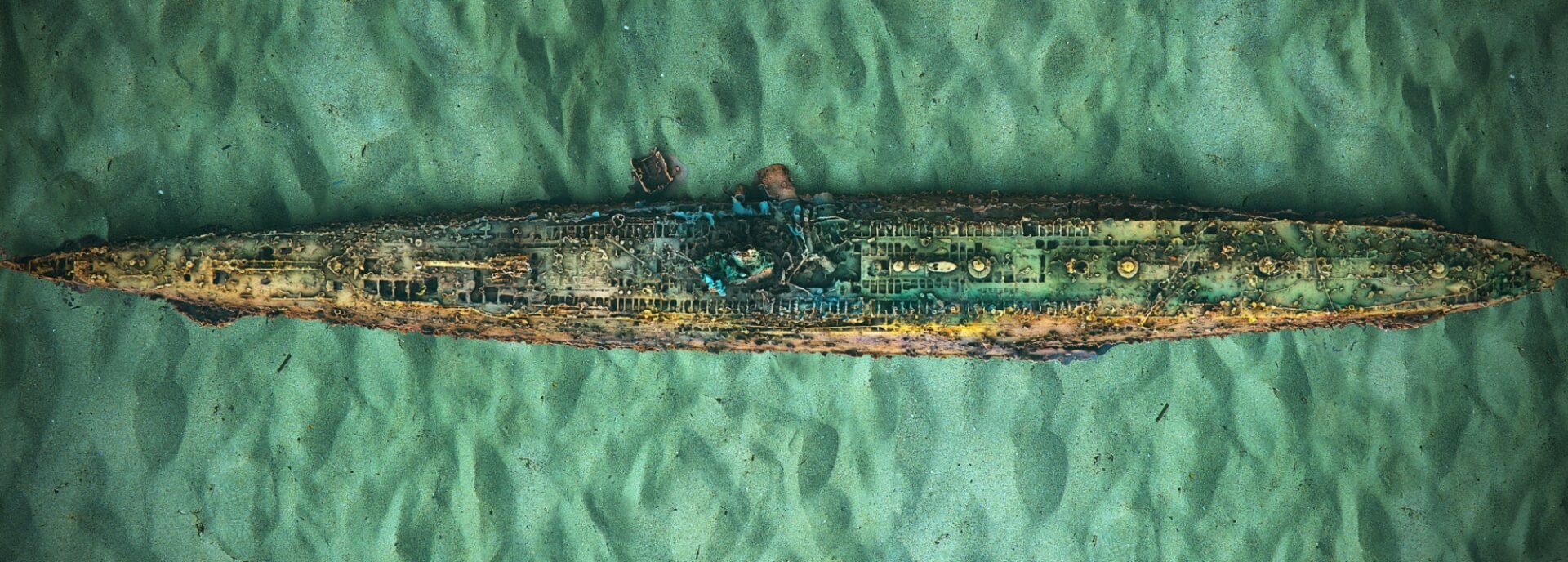 View of a wrecked submarine sitting on the seabed, in clear aqua-coloured water