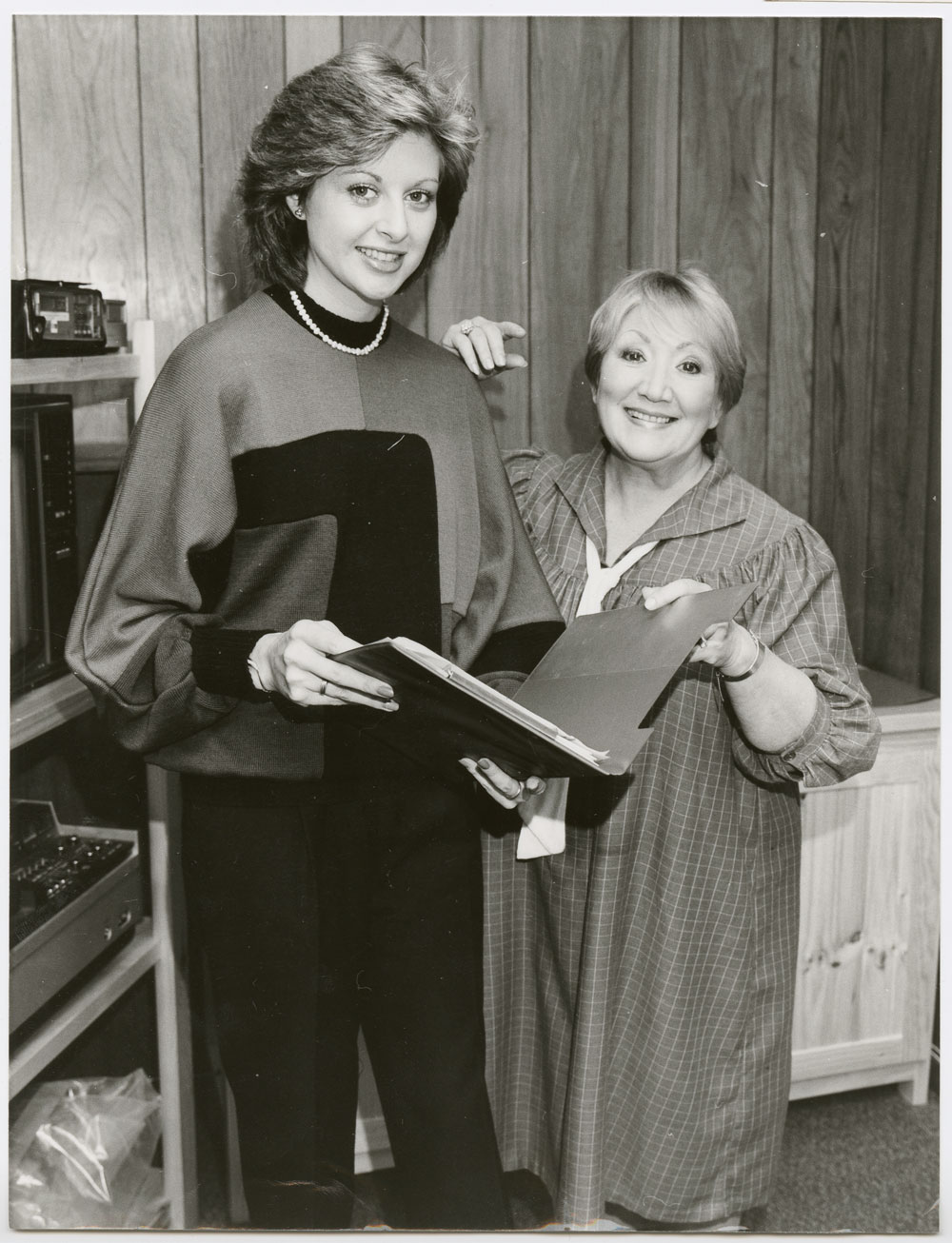Photograph of June Bronhill taken when she was a guest on the television program “Adelaide Today” hosted by Amanda Halvorse. June and Amanda stand next to each other holding open between them a folder with some papers.