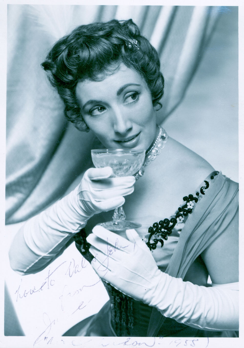 Formal portrait of June Bronhill taken in London in 1954. June wears long white Opera gloves and holds a crystal goblet. There is a hand-written note on the lower right of the photo by June saying “Love to Val & John from June (illeg) 1955