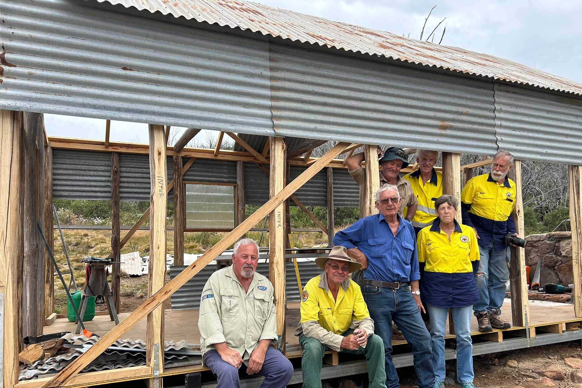 Chaps in uniformposing on edge of hut under construction.
