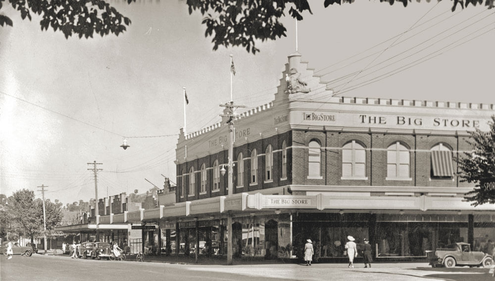 Black and white photo of The Big Store on Dean Street, Albury, circa 1950. The two-storey building is located on a street corner and photographed from a left diagonal angle across the road. Several cars are parked along the streets, and pedestrians are seen crossing the road, capturing a lively mid-century streetscape.