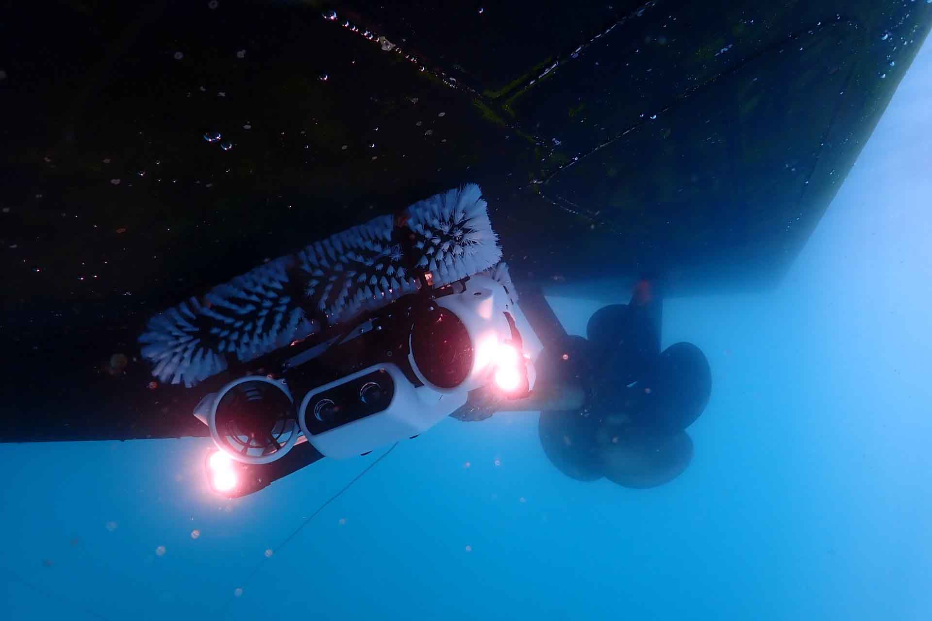 A robot cleaner crawls along the hull of a boat underwater.