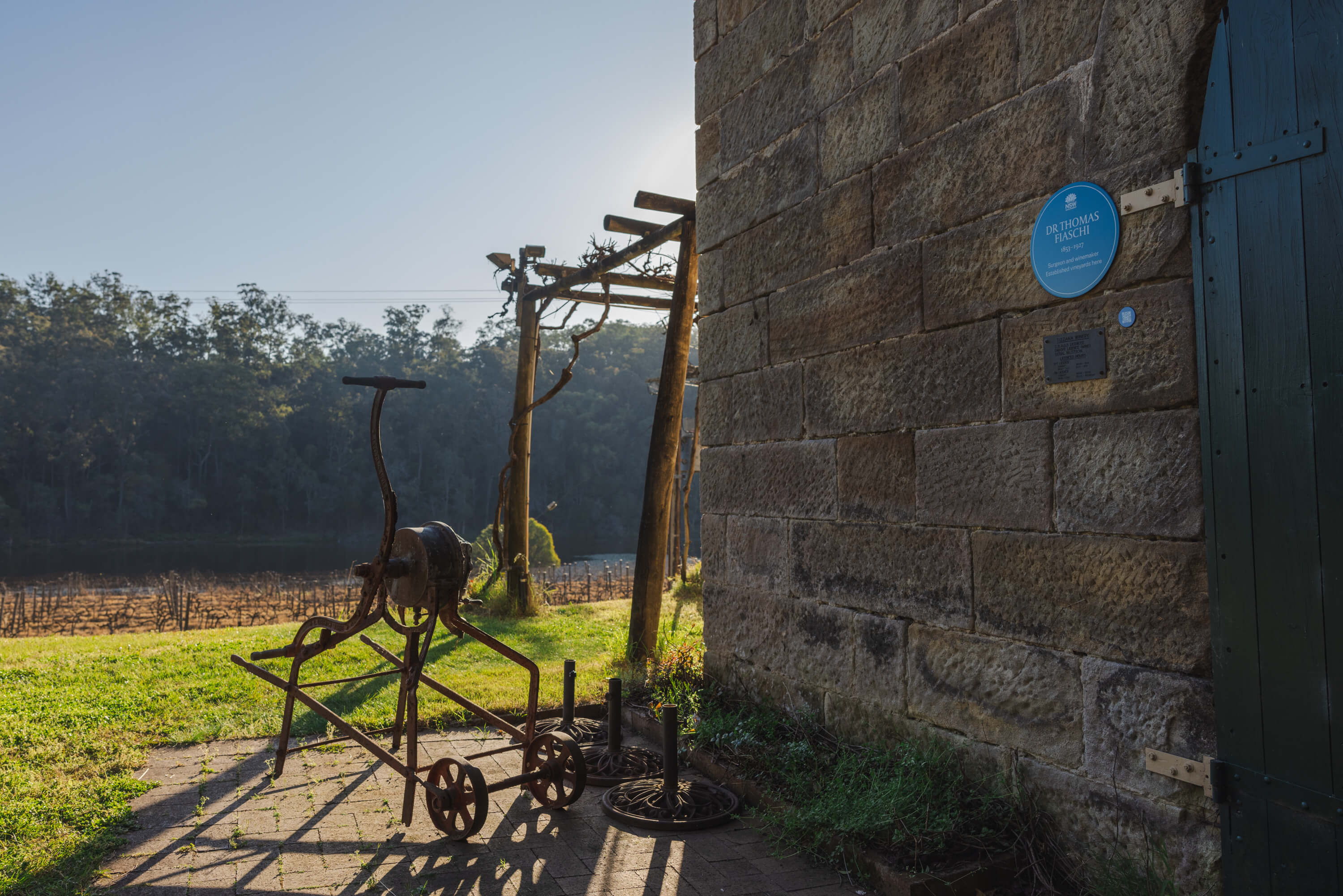 A picture of a blue plaque on a sandstone building with a vineyard in the background