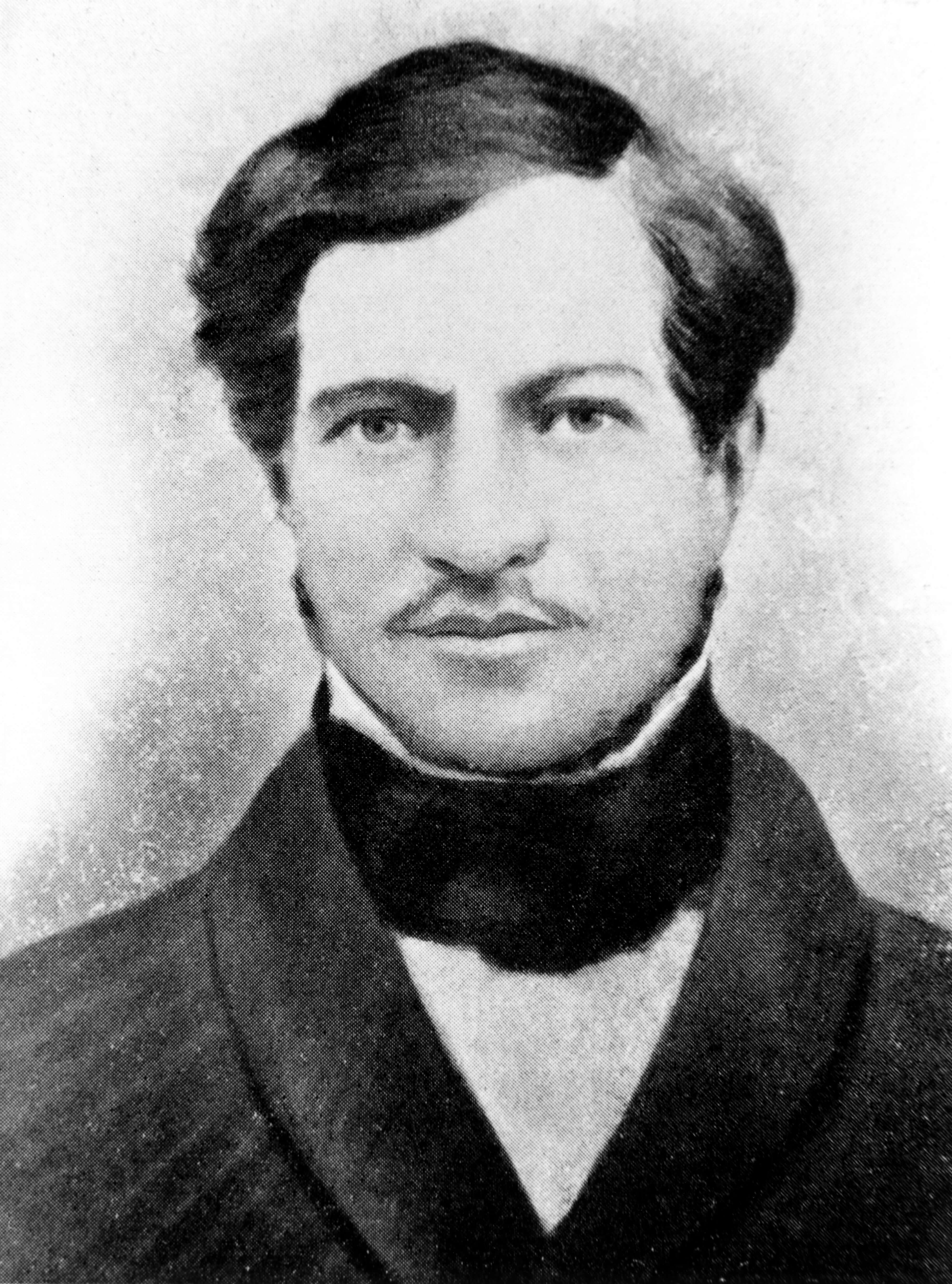 A black and white image of man's face. The man is wearing a suit and has a moustache.