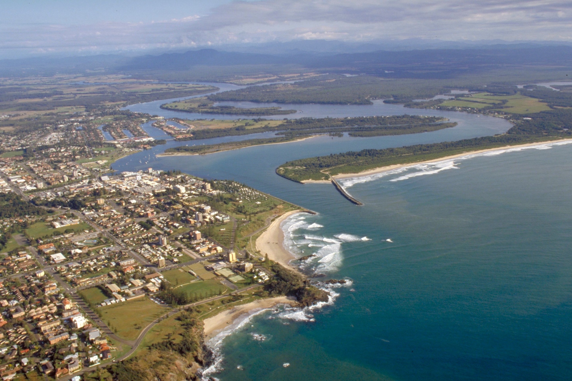 A river estuary next to a town, with forest and distant mountains in the background