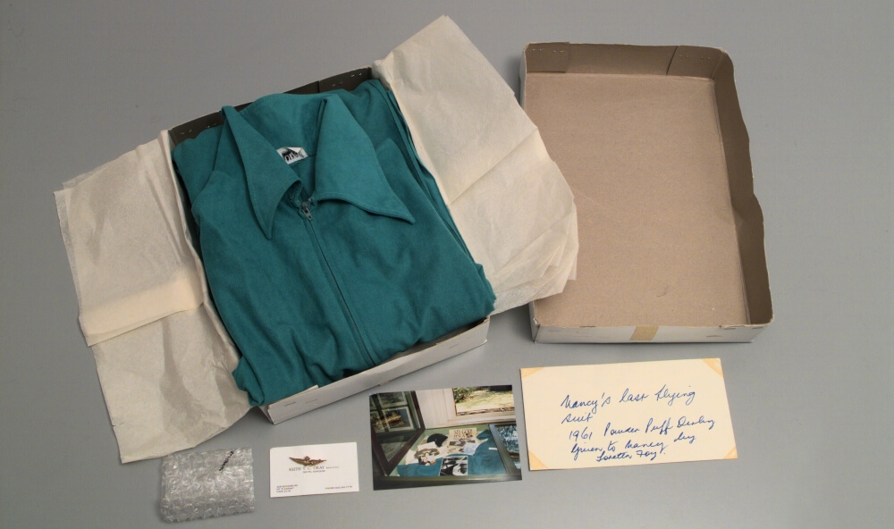 A blue flying suit, a badge and related materials lying on a table