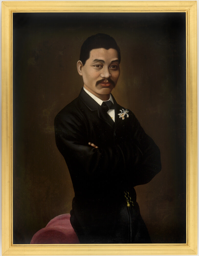Portrait of Mei Quong Tart in a tuxedo and bow tie, leaning on a pink chair.