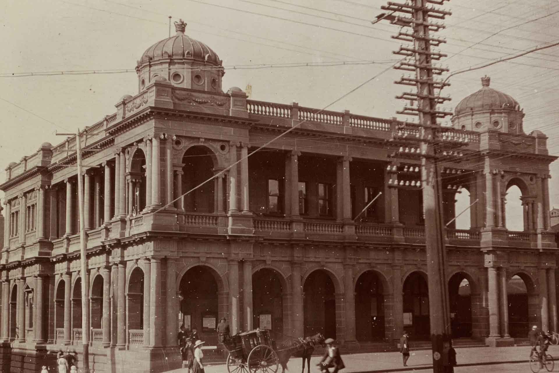 An ornate 2 storey stone building with columns, wrapping veranda and 2 towers with portholes. Photo taken approximately 1917-18  judging by the hats and collars and greater number of women and young boys.