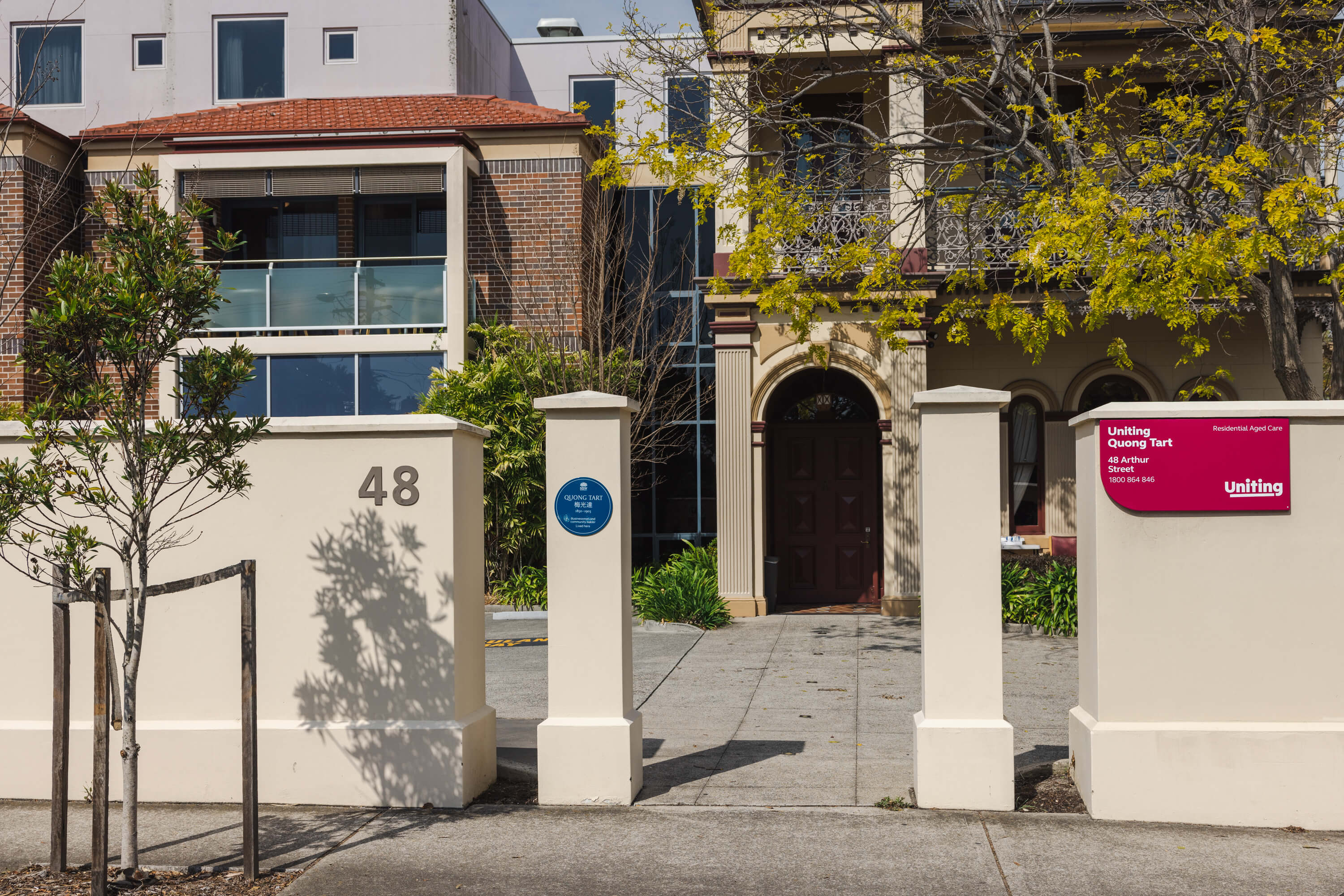 A photo of a blue plaque on a pillar out the front of a large house