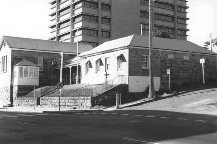 Old building with veranda, tower block in background. 