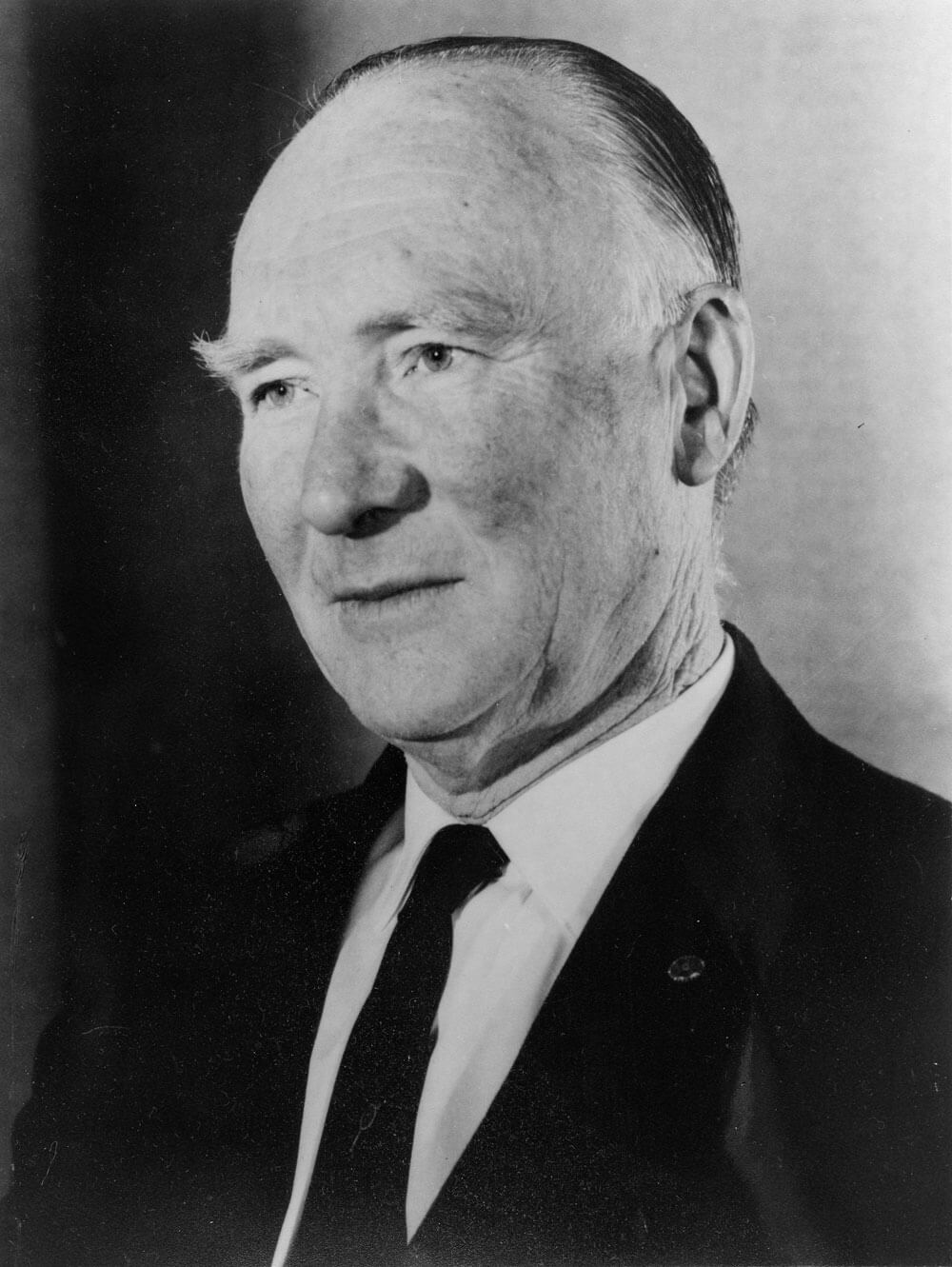 A black and white photograph of Thomas Leech in a dark suit and tie.