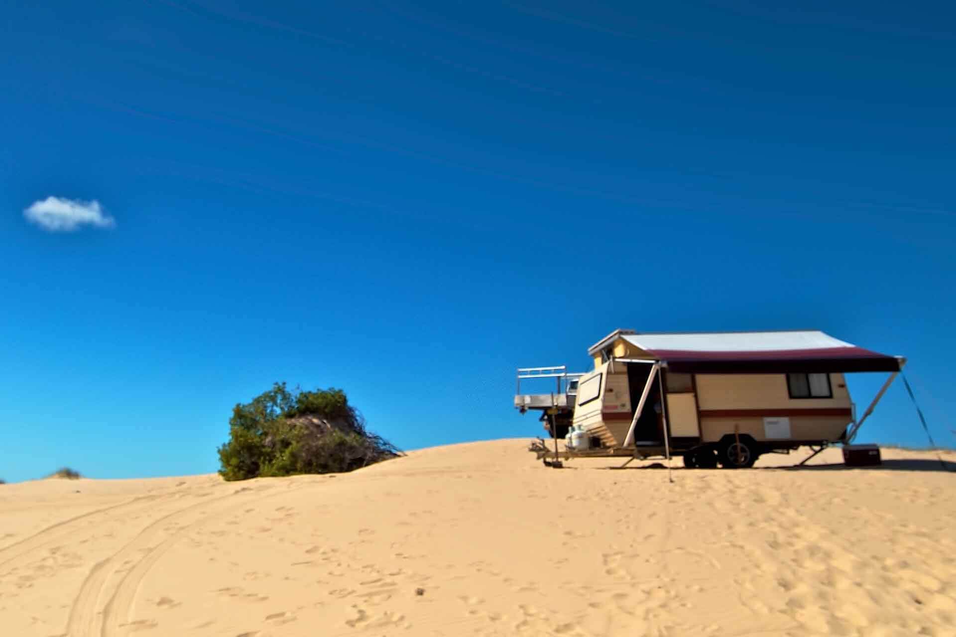 A caravan sits atop a dune, blue sky behind