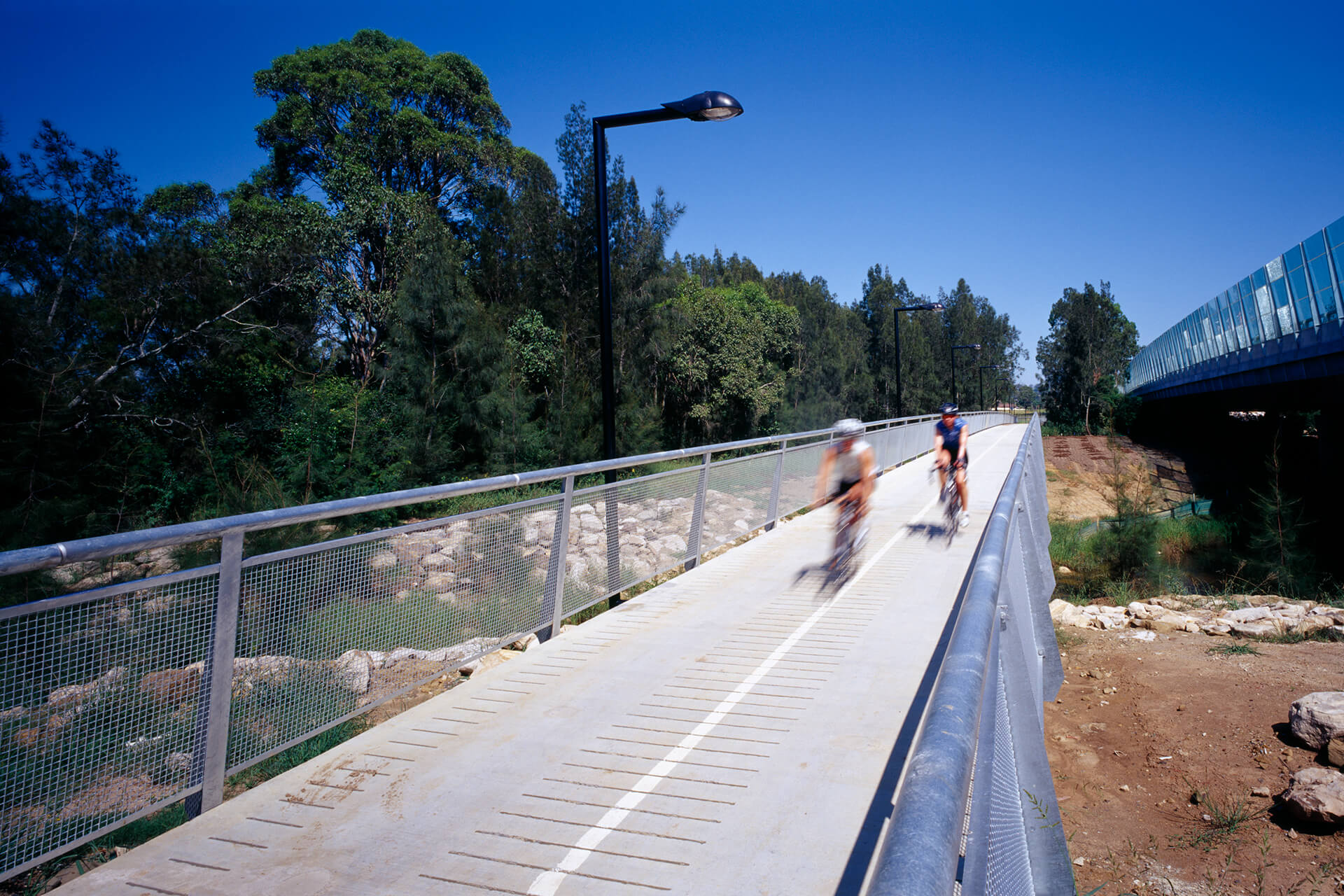 Two people on a fenced bike path travel through a barren landscape.