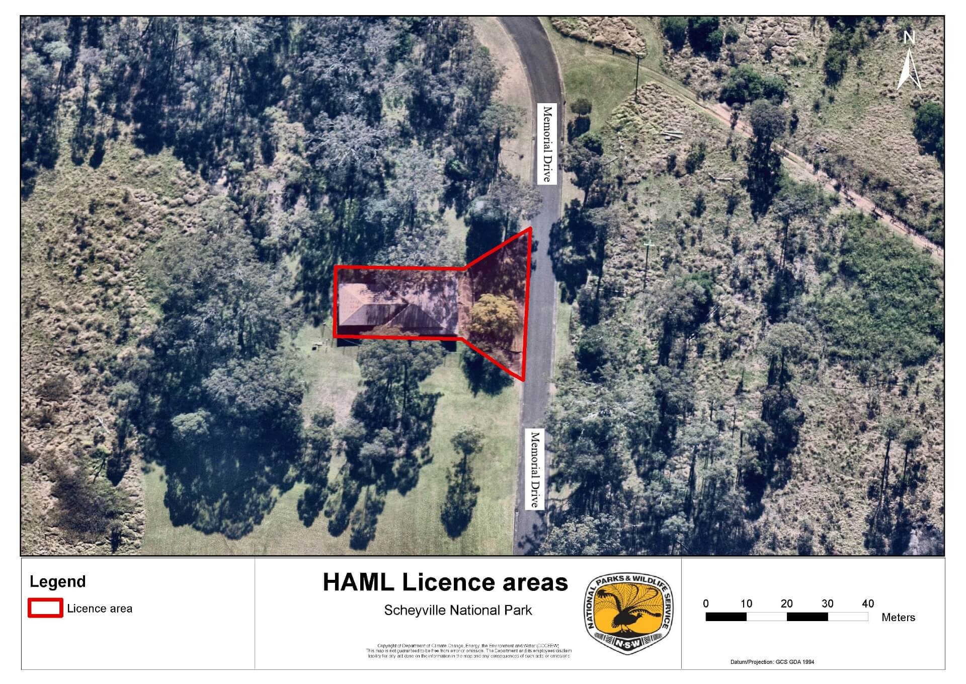 Aerial view of a small building, road and surrounding land. The building and area between it and the road are outlined in red to signify the lease area.