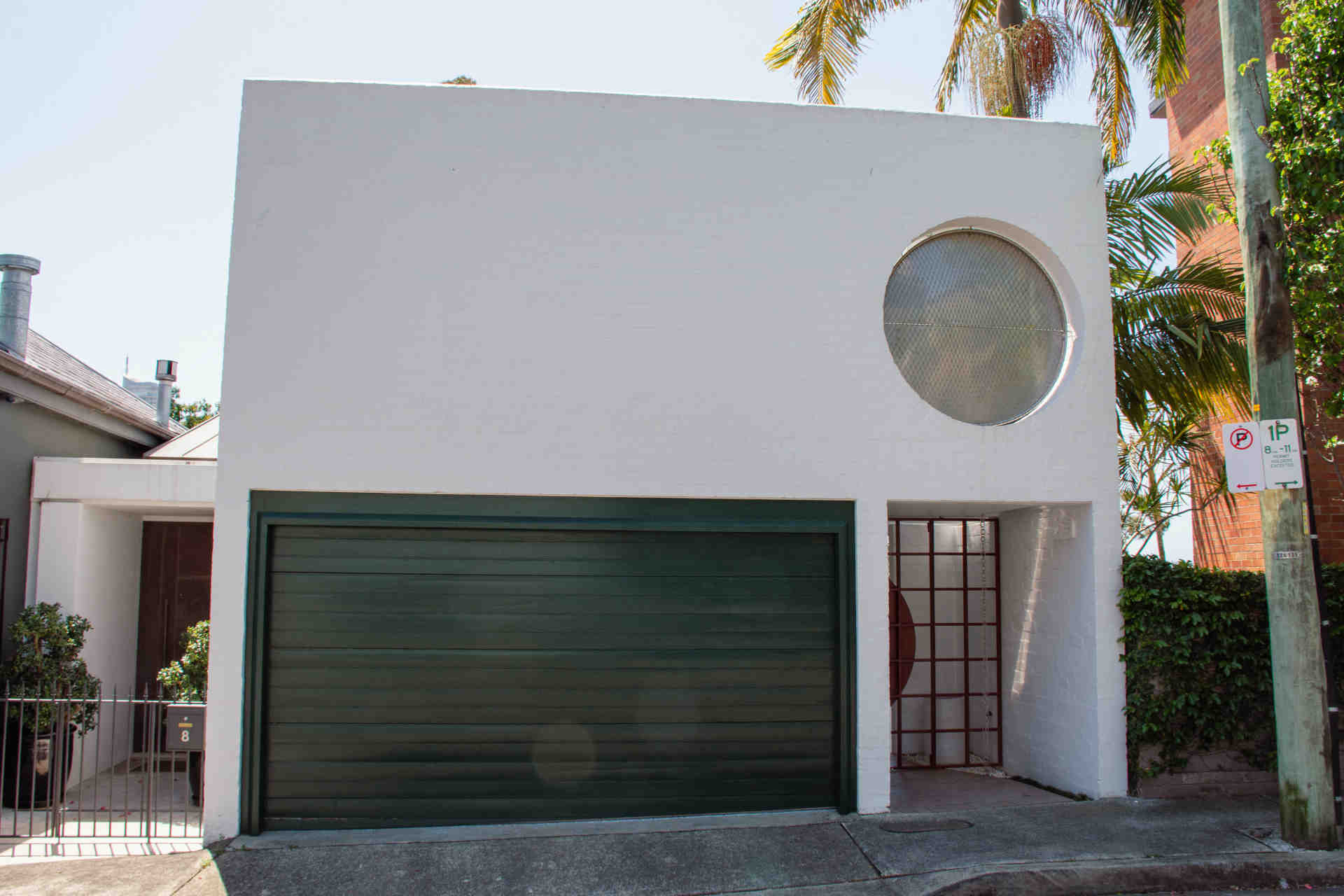 A photo showing the front exterior of Woolley Townhouse, a white two-storey residential building with fenced front door and garage door painted in dark green  