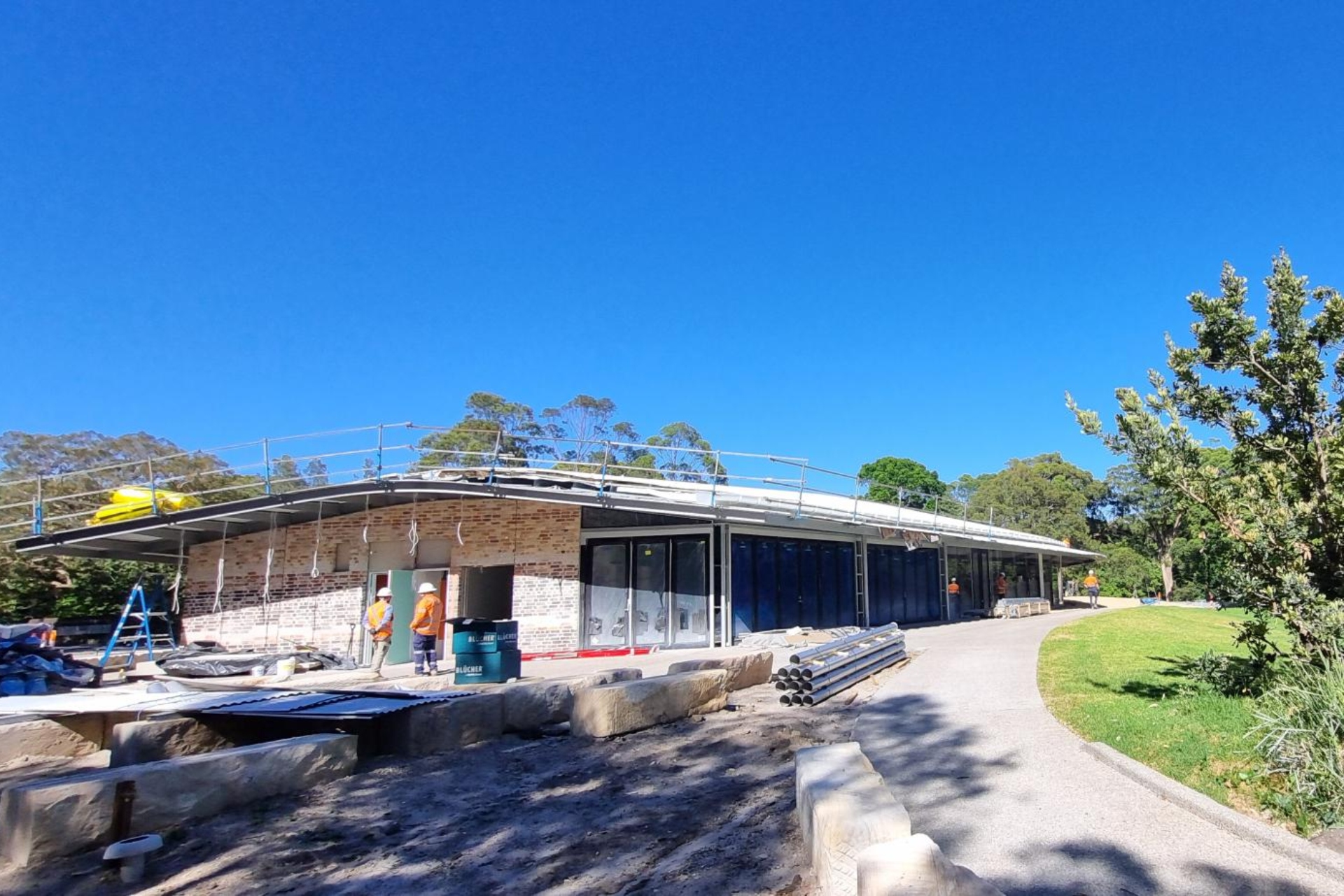 A concrete footpath leads to a single-storey brick building with scaffolding around its edges