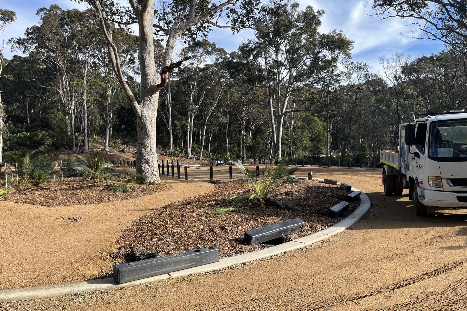 View of curved edging with infill and vehicle visible, with trees in background.