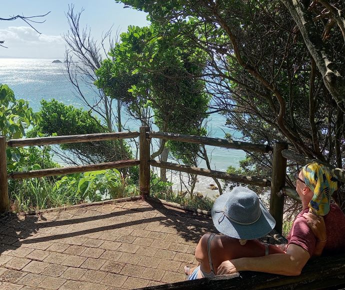 Two people sit on a bench looking at the ocean at one of the lookouts to be upgraded at Cape Byron State Conservation Area