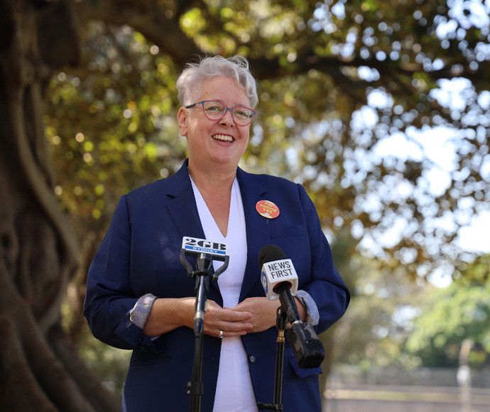 Minister for the Environment Penny Sharpe in front of a fig tree with dappled light coming through the leaves, and media microphones in foreground