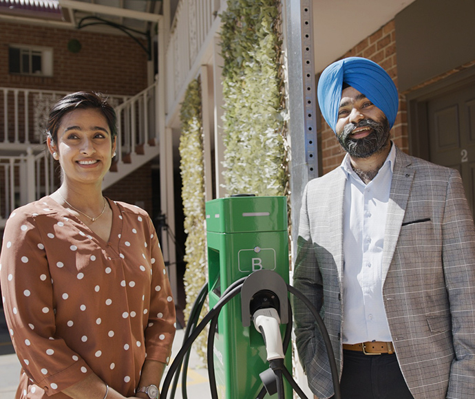 Woman in bown and white spooted dress, green EV charging station, man in checked jacket.