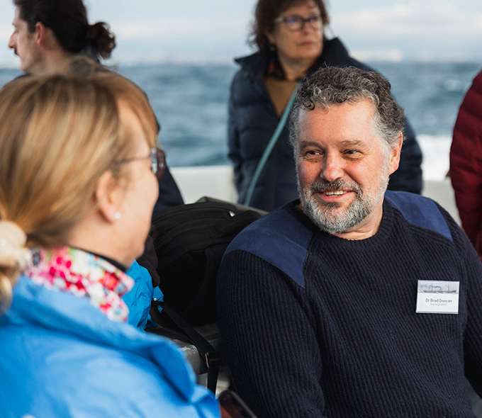 Dr Brad Duncan, Senior Assessments Officer, Heritage NSW, wearing name tag, talking while on a boat at sea