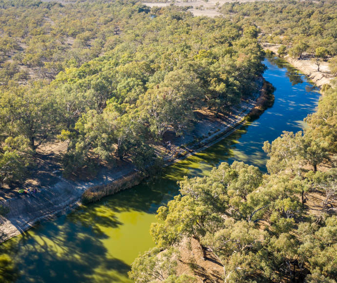 Aerial photograph of a still, narrow river with dry-looking banks of thick eucalypt forest
