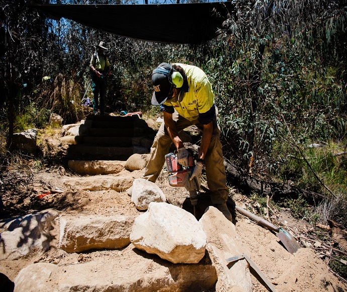 Male construction working in centre frame working on walking track.