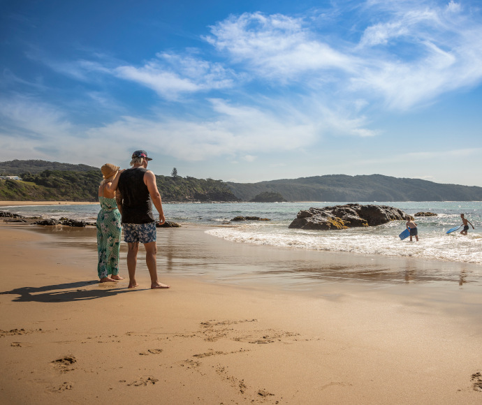 Two adults watching two children play in the water at Boat Beach, Myall Lakes National Park