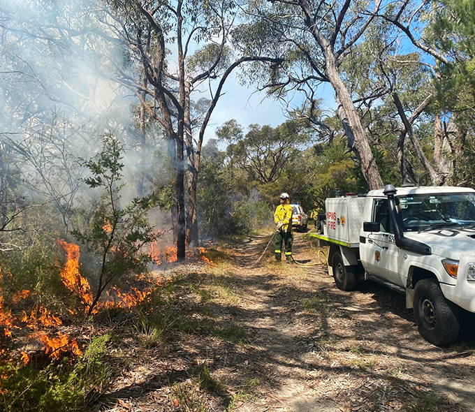 Man with protective gear standing by truck, observing fire