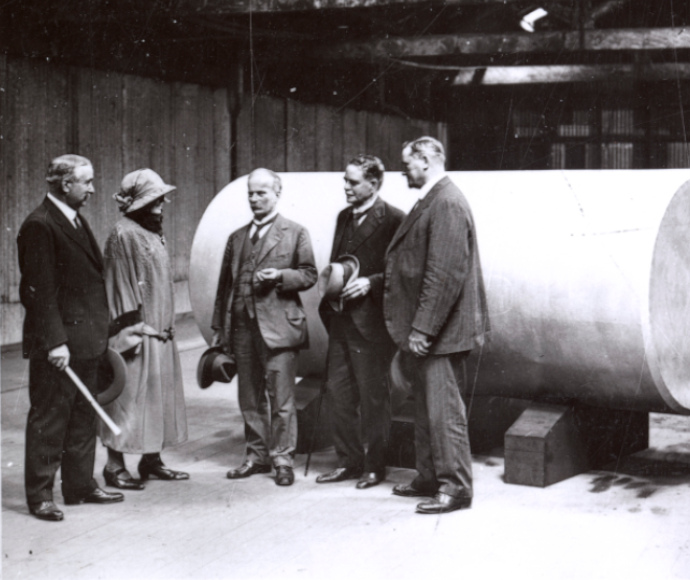 Grainy 1920's black and white photograph of three men and a woman standing next to a large concrete pole.